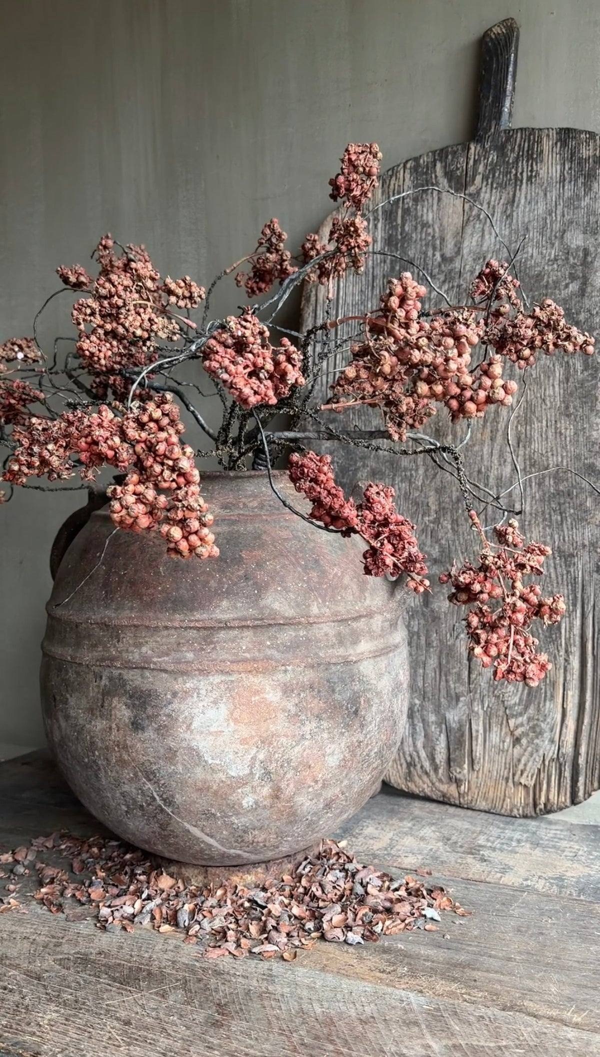 Kunstboeket ligustrum met dusty red bessentakken en takkenbos in een oude stenen pot